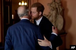 FILE - Britain's Prince Harry kisses and greets his father, then-Prince Charles, upon their separate arrival to attend a coral reef health and resilience meeting at Fishmongers Hall in London on Feb. 14, 2018.