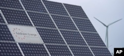 The logo of the 'Feldheim Energie' (Feldheim Energy) company is framed by solar panels in Feldheim near Treuenbrietzen, Germany, Wednesday, Sept. 28, 2022. (AP Photo/Michael Sohn)