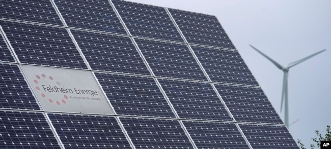 The logo of the 'Feldheim Energie' (Feldheim Energy) company is framed by solar panels in Feldheim near Treuenbrietzen, Germany, Wednesday, Sept. 28, 2022. (AP Photo/Michael Sohn)