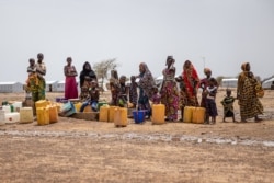 FILE - Women queue at the water pump in Goudoubo, a camp with about 11,000 refugees, in northern Burkina Faso, June 20, 2021.