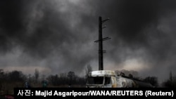 8일(현지시간) 이란 테헤란의 샤한 연료 탱크가 공격을 받아 파괴된 차량 뒤로 검은 연기가 솟구치고 있다. [사진 제공: 마지드 아스가리푸르/WANA 통신/로이터] 