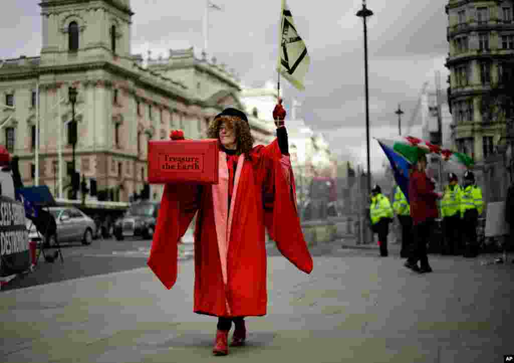 A woman dressed as the Speaker of the House of Commons holds a case with a message &#39;treasure the earth&#39; as she participates in a demonstration on the budget outside Parliament in London.