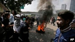 Para pengunjuk rasa beristirahat dekat sebuah ban yang terbakar setelah bentrok dengan polisi dalam demonstrasi memprotes hasil rekapitulasi pilpres di Jakarta, Rabu, 22 Mei 2019. (Foto: AP/Dita Alangkara)