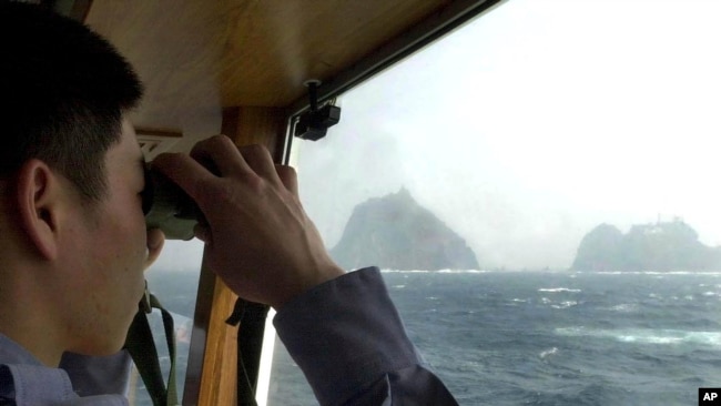 一名韩国海岸警卫队员在韩国东海的巡逻舰上用望远镜观察“独岛”（日本称之为“竹岛”）（2005年4月28日照片）
