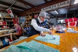 In this March 23, 2020, photo, Karen Haley cuts cotton fabric for masks to be given to caregivers during the coronavirus outbreak, at the North Sails shop in Freeport, Maine.