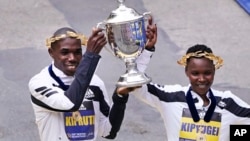 Benson Kipruto, kiri, dan Diana Kipyogei, kanan, keduanya dari Kenya, merayakan di garis finis setelah memenangkan Boston Marathon divisi putra dan putri di Boston, 11 Oktober 2021. (Foto: AP)