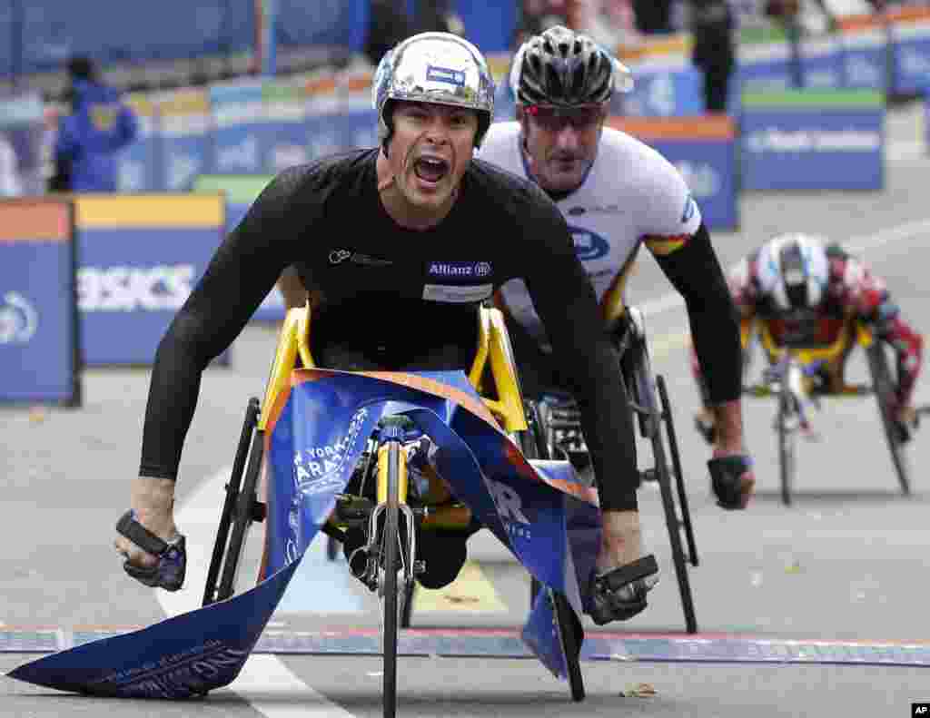 Marcel Hug of Switzerland reacts crossing the finish line followed by Ernst Van Dyk of South Africa, center, and Kurt Fearnley of Australia, right, as he wins the mens' wheelchair division during the New York City marathon, in New York. 
