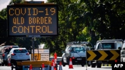 A COVID-19 signage is seen at a vehicle checkpoint on the Pacific Highway on the Queensland - New South Wales border in Brisbane on April 15, 2020. - A state border that bisects Australia's neighbouring beachside towns of Coolangatta and Tweed…