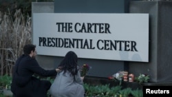 Una mujer sostiene flores frente al cartel del Centro Presidencial Carter, después de la muerte del expresidente estadounidense Jimmy Carter a la edad de 100 años, en Atlanta, Georgia, EEUU, el 29 de diciembre de 2024.