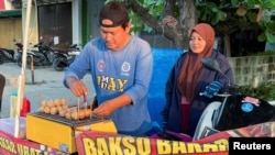 FILE - Rahmat Hidayat serves a customer as he grills meatball after losing his job when the shoe factory he worked for closed down last year in Karawang, West Java Province, Indonesia, July 31 , 2024.