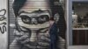 A man wearing a protective face mask walks past graffiti by Greek street artist Achilles in central Athens, May 8, 2020.