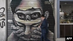 A man wearing a protective face mask walks past graffiti by Greek street artist Achilles in central Athens, May 8, 2020.