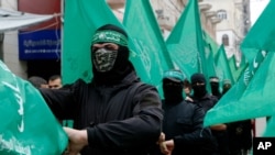 Masked Hamas militants wave green flags during a protest in Gaza City, Feb. 14, 2020. Arabic on the headband reads: "No God but Allah and Muhammed is his messenger, al-Qassam Brigades."