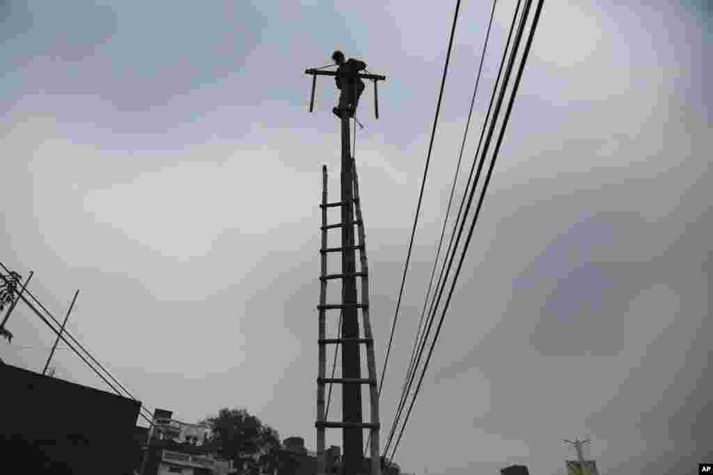 An Indian electricity department worker climbs on a pole to fix power lines as monsoon clouds gather above in Jammu.