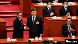 El presidente de China, Xi Jinping (centro), da la mano al recién elegido primer ministro Li Qiang (izquierda) mientras el exprimer ministro Li Keqiang (derecha) aplaude durante la cuarta sesión plenaria de la Asamblea Popular Nacional (APN), en Beijing, el 11 de marzo de 2023.