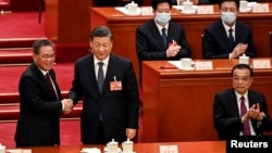 中国领导人习近平和新总理李强在全国人大会议期间握手，李克强在旁。（2023年3月11日）