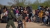Migrantes centroamericanos con niños esperan en un campo de béisbol después de cruzar el Río Grande hacia EE. UU. en balsas, en La Joya, Texas, el 19 de marzo de 2021.