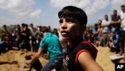 FILE - In this Monday, Aug. 4, 2014 file photo, mourners gather around the graves of members of the Najam family, killed overnight in an Israeli strike in Beit Lahiya, Gaza Strip.