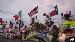 FILE - Flags fly over crosses at a makeshift memorial near the scene of a mass shooting, Aug. 4, 2019, at a shopping complex in El Paso, Texas, Aug. 6, 2019.