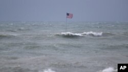 Una bandera estadounidense ondea desde el lugar del naufragio del Breconshire, mientras las olas agitadas por la tormenta tropical Isaias chocan a su alrededor, el domingo 2 de agosto de 2020, en Vero Beach, Florida.