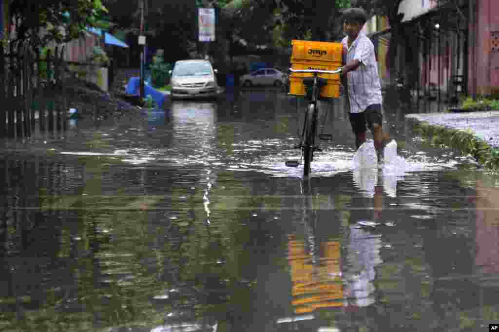 A man pushes his bicycle, carrying milk for sale, past a waterlogged street after rainfall during the monsoon season, in Mumbai, India.