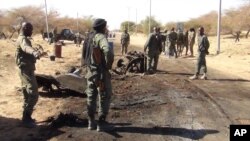 In this photo taken March 21, 2013, Malian soldiers stand around the debris left after a jihadist suicide bomber blew himself up at a Malian army checkpoint near the airport in Timbuktu, Mali.