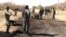 In this photo taken March 21, 2013, Malian soldiers stand around the debris left after a jihadist suicide bomber blew himself up at a Malian army checkpoint near the airport in Timbuktu, Mali.