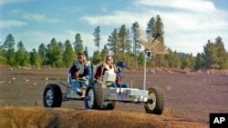 This undated photo provided by the U.S. Geological Survey Astrogeology Science Center shows Apollo 15 astronauts Jim Irwin, left, and Dave Scott driving a prototype of a lunar rover in a volcanic cinder field east of Flagstaff, Ariz. 