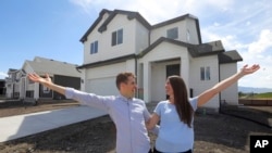 In this April 27, 2019, photo, millennials Andy and Stacie Proctor stand in front of their new home in Vineyard, Utah. 