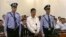 In this image taken from video, disgraced politician Bo Xilai, center, stands in the courtroom, flanked by police guards at Jinan Intermediate People's Court in eastern China's Shandong province, Aug. 22, 2013.