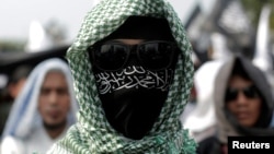 An Islamic group member covers his face with Hizbut Tahrir flag during a protest against the decree allowing the government to disband organizations deemed to run counter to the secular state, in Jakarta, Indonesia, July 28, 2017. 