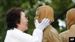 FILE - Lee Yong-soo who was forced to serve as a sex slave for Japanese troops during World War Two, touches the face of a statue symbolizing the issue of wartime 'comfort women' during its unveiling ceremony in Seoul, South Korea, Aug. 14, 2019.
