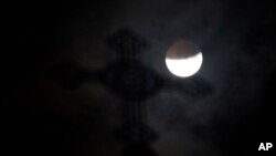 FILE - A church steeple is seen as the full moon is shadowed by the Earth during a partial phase of a total lunar eclipse on the arrival of the winter solstice.