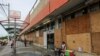 A woman waits for clients outside a supermarket with its windows covered with plywood as Tropical Storm Zeta approaches Cancun, Mexico, Oct. 26, 2020.