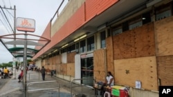 A woman waits for clients outside a supermarket with its windows covered with plywood as Tropical Storm Zeta approaches Cancun, Mexico, Oct. 26, 2020.