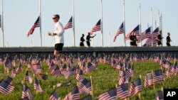 Morning joggers look over small flags that activists from the COVID Memorial Project placed on the grounds of the National Mall to mark the deaths of 200,000 lives lost in the U.S. to COVID-19, Sept. 22, 2020 in Washington.