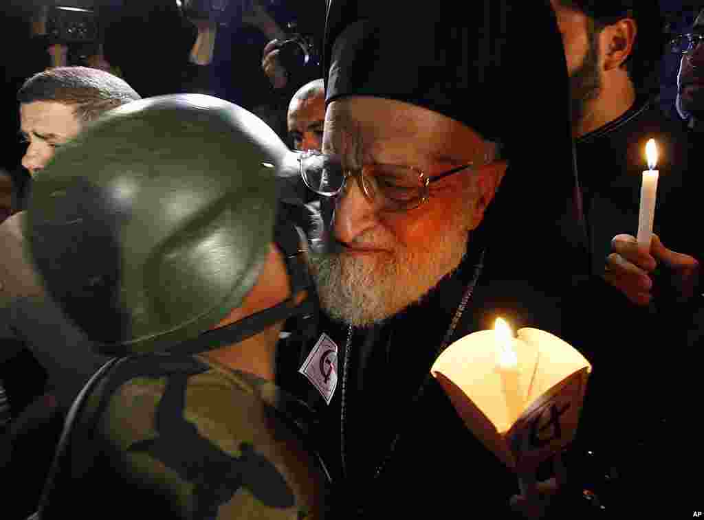 A Syrian army soldier, left, kisses Gregarious Laham, Patriarch of Antioch and the whole East for Roman Catholics, right, during a during a vigil for civilians and security officers killed in Saturday explosions in  Damascus.  (AP) 
