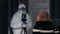 A security personnel wearing protective clothing to help stop the spread of a deadly virus which began in Wuhan, uses an advanced thermo camera to scan a woman (R) at a subway station entrance in Beijing on January 27, 2020. - China on January 27…