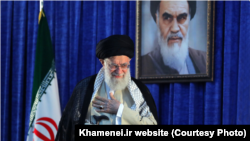 Iranian Supreme Leader Ayatollah Ali Khamenei gestures to a crowd at a June 4, 2019 ceremony in Tehran marking the 30th anniversary of the death of his predecessor, Ayatollah Ruhollah Khomeini, whose portrait appears behind him.