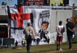 FILE - Demonstrators unfurl a banner with a cartoon image of Brazil's President Jair Bolsonaro with a paintbrush, insinuating he transformed a red cross into a swastika, during an anti-Bolsonaro protest, in Brasilia, Brazil, June 21, 2020.