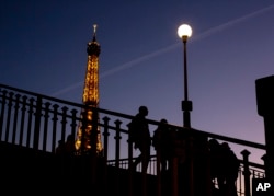 FILE - People walk on a bridge next to the Eiffel Tower in Paris, Wednesday Feb. 9, 2022. Lights on the Eiffel Tower will soon be turned off an hour earlier at night as part of an energy savings plan in the French capital, its mayor announced. (AP Photo/Rafael Yaghobzadeh, File)