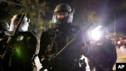 FILE - Portland police officers walk through the Laurelhurst neighborhood after dispersing protesters from the Multnomah County Sheriff's Office early in the morning, Aug. 8, 2020 in Portland, Oregon.