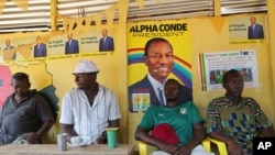 People sit inside a local restaurant displaying posters for Guinea’s incumbent President Alpha Conde, in Conakry, Guinea, Oct. 17, 2015.