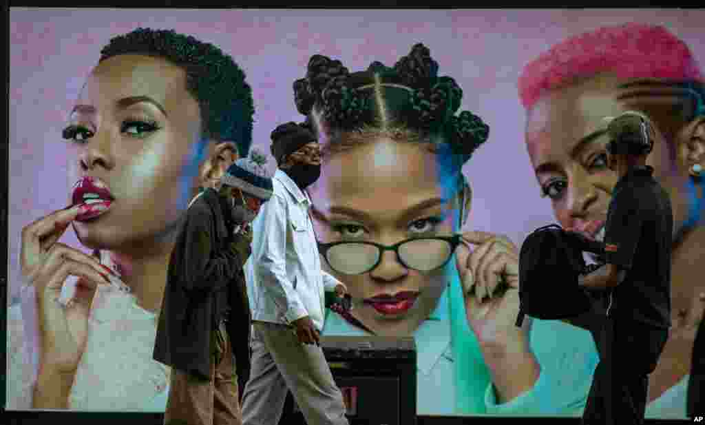 Men wearing face masks walk past a hair product billboard on the street in Soweto, South Africa, June 29, 2020.