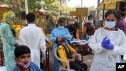 A health worker takes a nasal swab sample of a woman to test for COVID-19 near the landmark Gateway of India in Mumbai, India, April 5, 2021. 