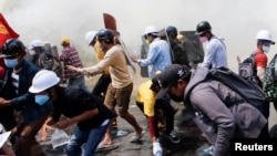 FILE - Tear gas and fire extinguisher gas surround demonstrators as they run away from police during a protest against the military coup in Naypyitaw, Myanmar, March 8, 2021.
