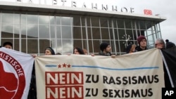 Quelques personnes manifestent en face de la gare centrale de Cologne, en Allemagne, le mercredi 6 janvier 2016, avec une affiche mentionnant : "Non au racisme, Non au sexisme".