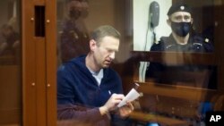 Pemimpin oposisi Rusia Alexei Navalny menulis catatan saat menghadiri sidang atas tuduhan pencemaran nama baik di Pengadilan Distrik Babuskinsky di Moskow, Rusia, 12 Februari 2021. (Babuskinsky District Court Press Service via AP)