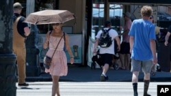 A person uses an umbrella for shade from the sun while walking near Pike Place Market, June 29, 2021, in Seattle. 