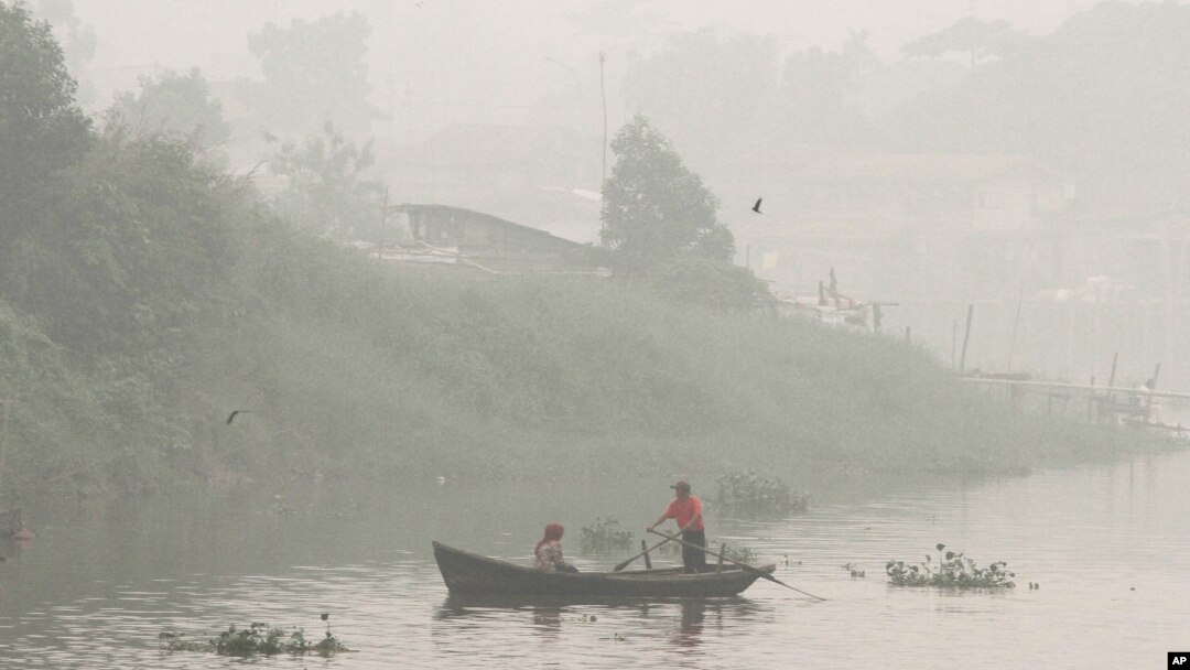 Warga mendayung perahu di Sungai Siak yang diselimuti kabut asap akibat kebakaran hutan di Pekanbaru, Riau (Oktober 2015). 